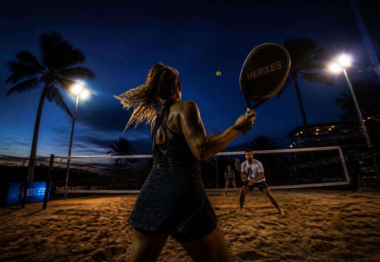 Atletas jogando beach tennis em quadra iluminada à noite